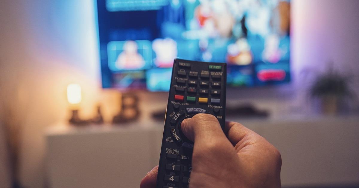 Hand holding remote control aimed at a television screen.