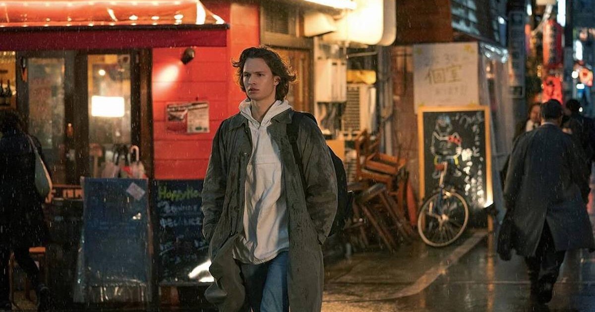 Jake Adelstein (Ansel Elgort) walks through a rainy Tokyo street on his way home from pursuing a story. Cr. WarnerMedia